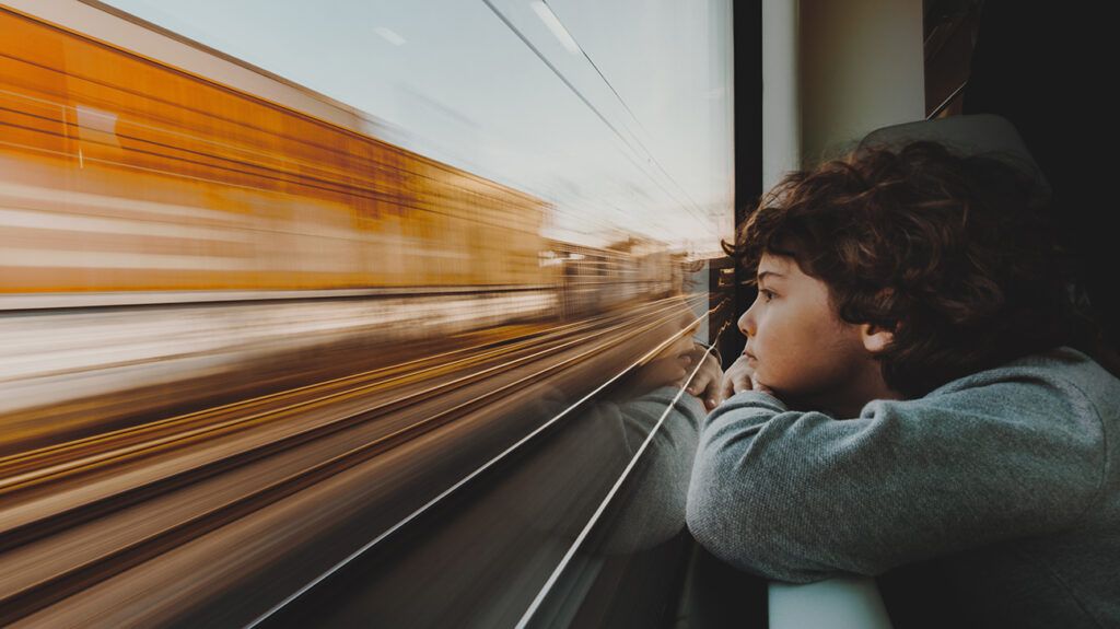 young child looking out window of moving train