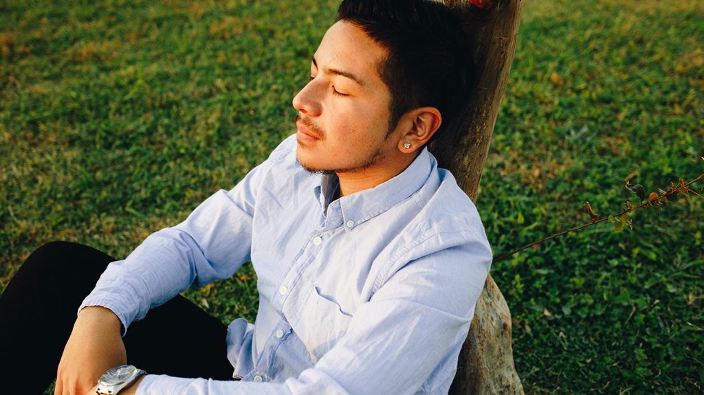 man sitting against a tree trunk, relaxed