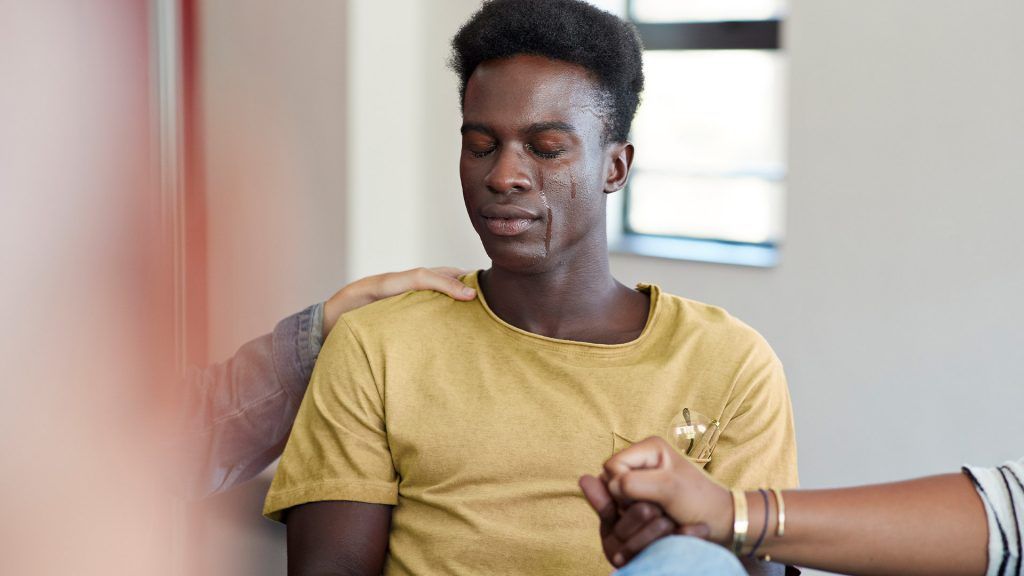 young man crying with eyes closed in group therapy