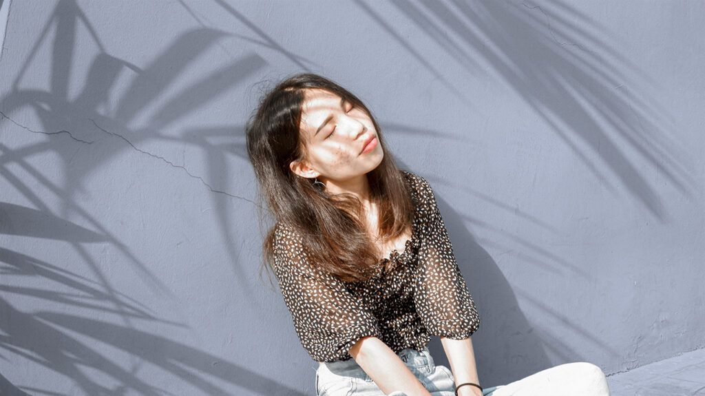 Young woman sitting against a wall with sunshine in her face